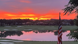 A golf course with a flagpole, water hazards, and distant buildings. - Luxury Villa Overlooking Lake Jovita's Championship Golf Course (Dade City)