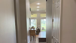 A hallway with a door, a wicker bench, and a view of a patio area. - Luxury Villa Overlooking Lake Jovita's Championship Golf Course (Dade City)