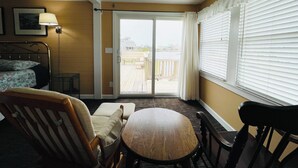Quarto de hotel com cama, cadeira, mesa, janela com persianas e vista para o terraço exterior.