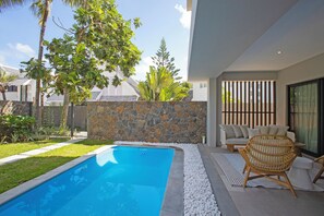 A swimming pool with a stone wall, white pebbles, and a wicker chair. - Villa Andrella - Beach Haven (Pointe d'Esny)