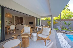 Ein moderner Außenbereich mit Korbmöbeln, einem Pool und Blick ins Innere.