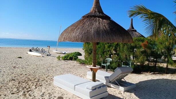 A beach with lounge chairs, a thatched umbrella, and a boat. - Villa Andrella - Beach Haven (Pointe d'Esny)