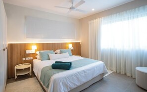 Ein Hotelzimmer mit Bett, Nachttischen, Deckenventilator und einem großen Fenster mit Vorhängen.