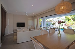 Una sala de estar moderna con sofá, televisión, mesa de comedor y sillas de mimbre.