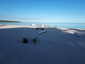 A beach with kayaks and a boat, clear blue water, and a distant shoreline. - Villa Andrella - Beach Haven (Pointe d'Esny)
