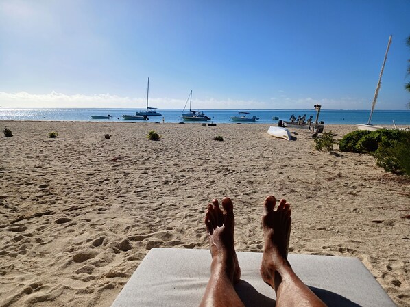 En sandstrand med liggestole og både i baggrunden.