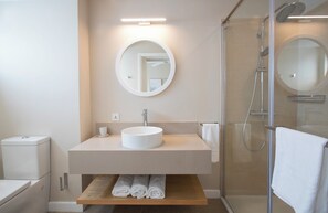 A bathroom with a round mirror, a sink, a shower, and a towel rack. - Villa Andrella - Beach Haven (Pointe d'Esny)