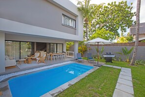 Et moderne hus med swimmingpool, udendørs møbler og grillområde.