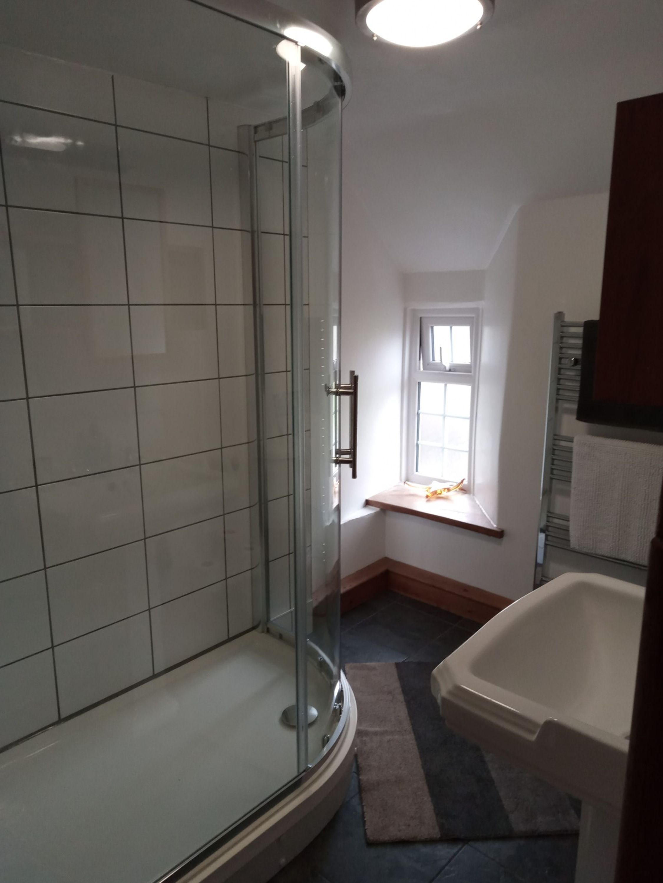 Un baño con ducha de vidrio, bañera blanca y ventana que proporciona luz natural.