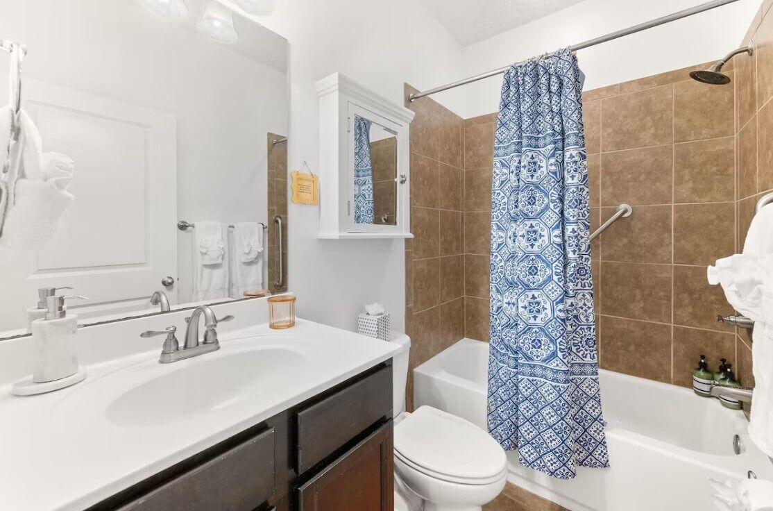Un baño con lavamanos blanco, espejo y cortina de ducha con diseño azul.
