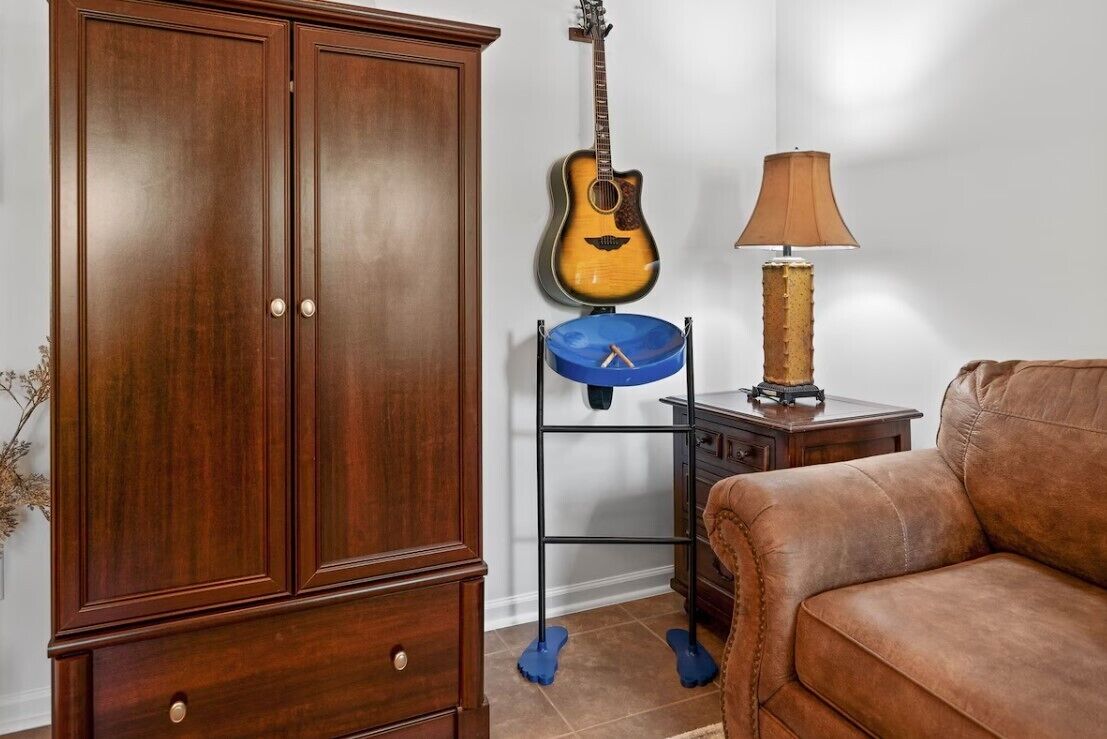 Ein Zimmer mit einem Holzschrank, einer Gitarre, einem blauen Waschbecken auf einem Metallständer, einer Lampe und einem braunen Ledersofa.