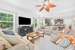Ein geräumiges Wohnzimmer mit großem Fernseher, Deckenventilator und Blick ins Freie.
