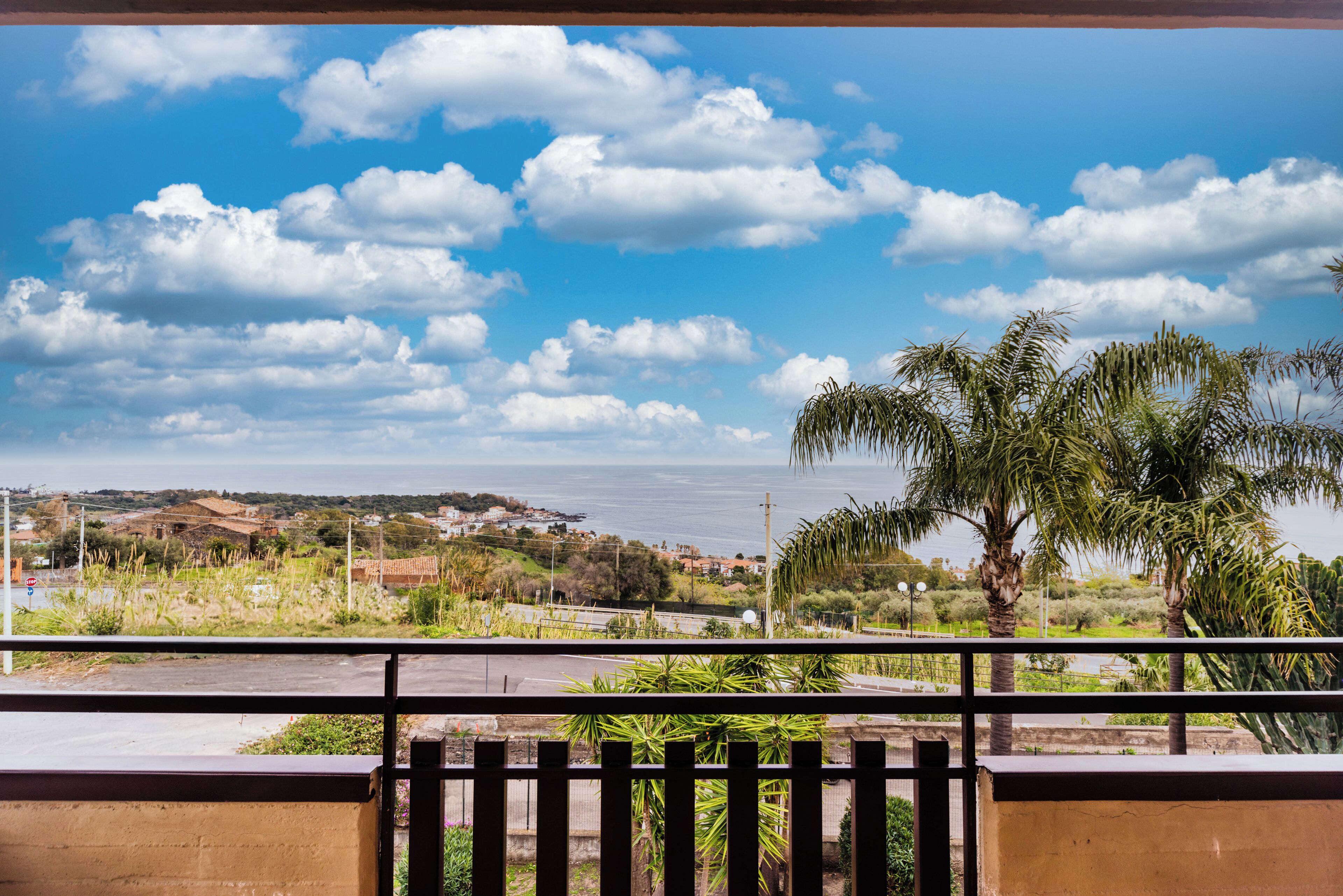 Un balcón con vista a un paisaje costero, palmeras y edificios a la distancia.
