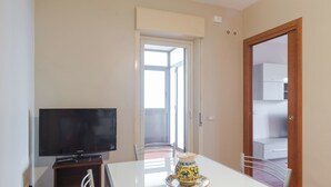 A room with a television on a stand, a dining table with chairs, and a door leading to a balcony. - Faraglioni Sea View Terrace by Wonderful Italy (Aci Catena)