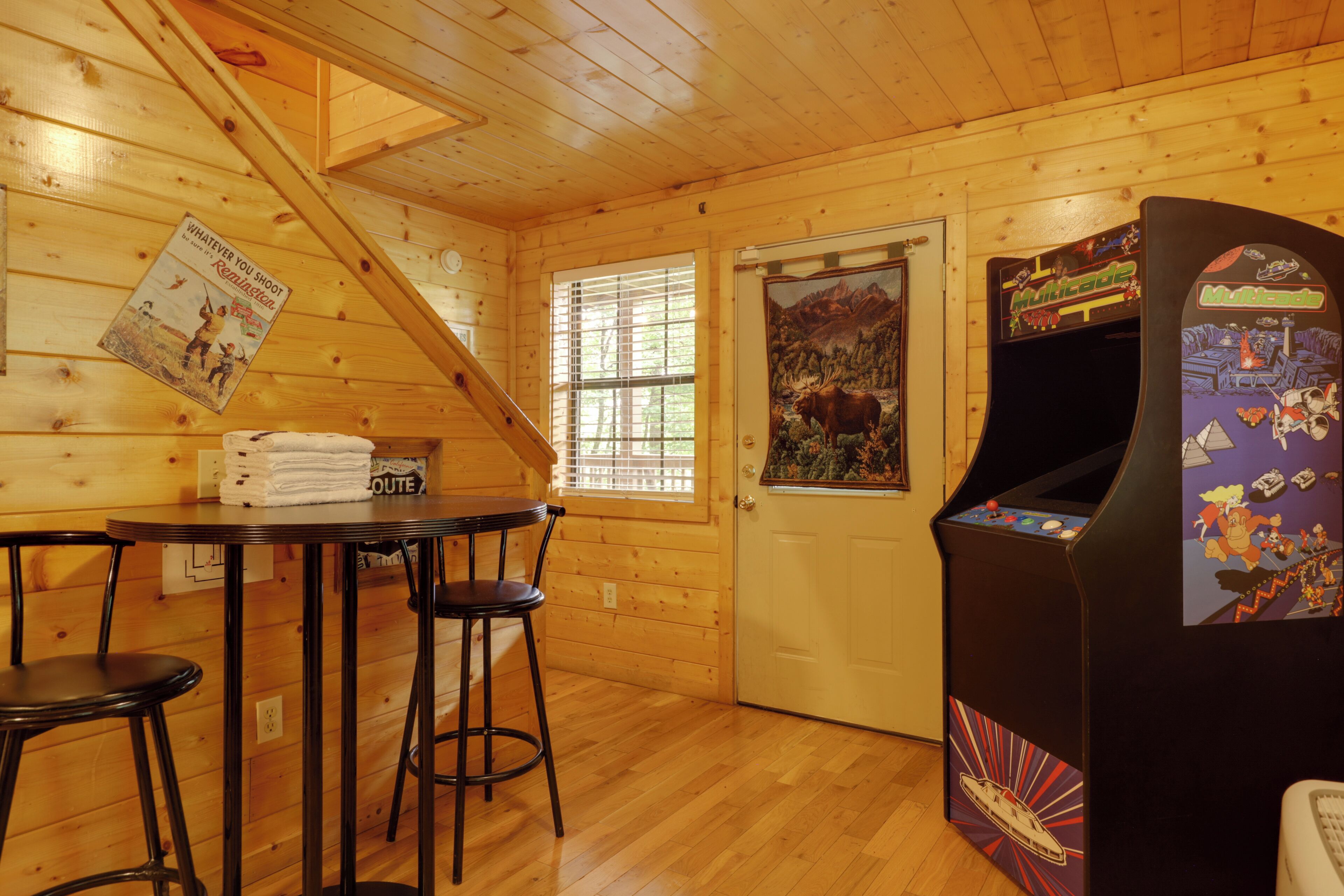 A wooden interior with a table, chairs, a door, and an arcade machine.