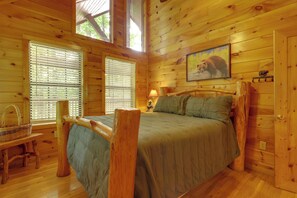 A wooden cabin bedroom with a bed, windows, a lamp, and a painting of a bear.