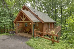 Une cabane en rondins avec un porche, une chaise et une petite terrasse.