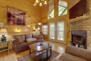 L’intérieur d’une cabane en rondins, avec une cheminée, des murs en bois, un canapé, une table basse et un ventilateur de plafond.