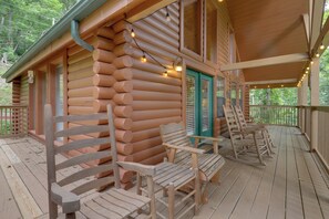 A log cabin with a porch, wooden rocking chairs, and string lights.