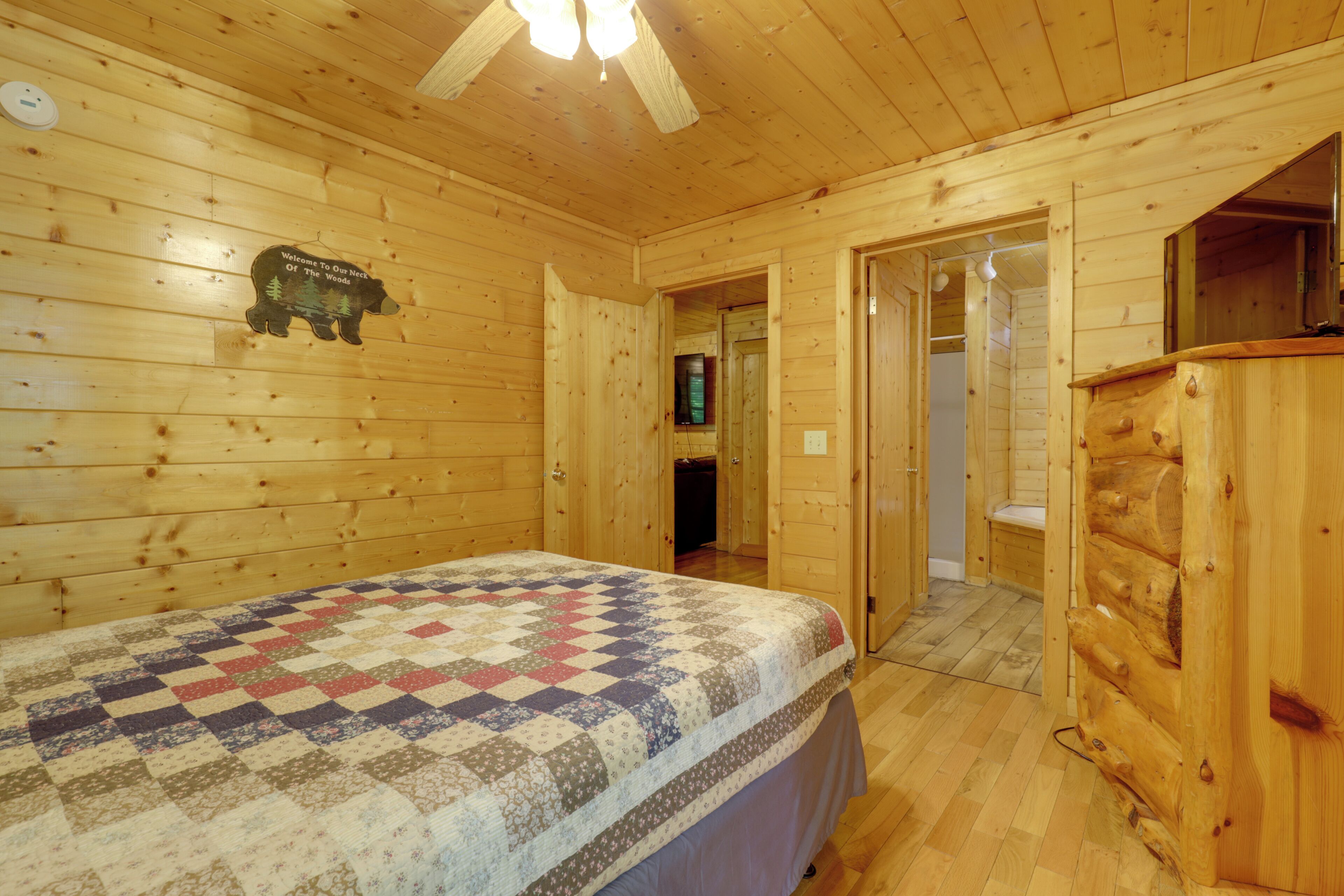 A wooden cabin bedroom with a bed, a dresser, and a door leading to another room.
