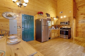 A wooden cabin interior with a kitchen featuring a refrigerator, microwave, stove, and wooden cabinets.