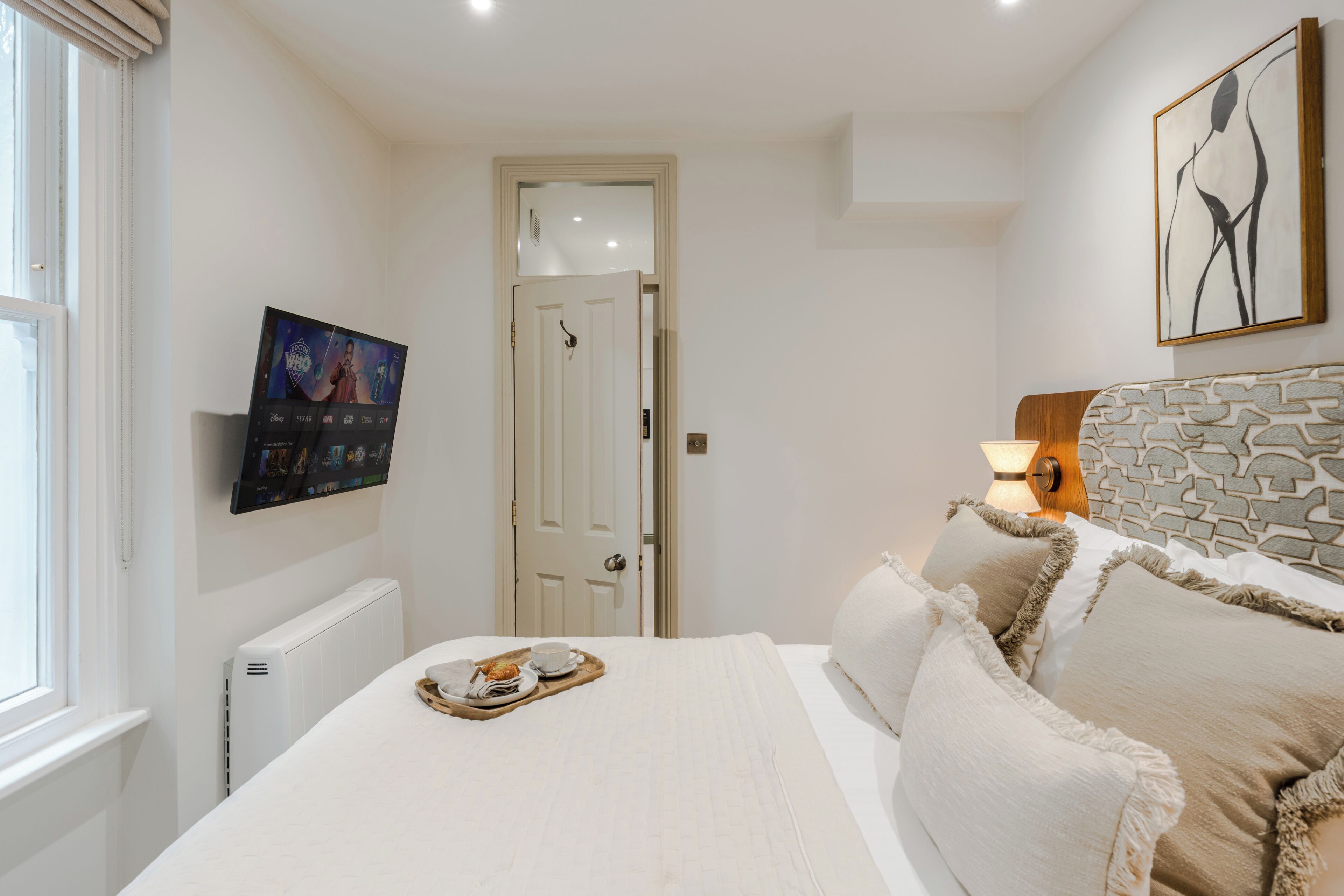 A bedroom with a bed, a television mounted on the wall, a door, and a painting.