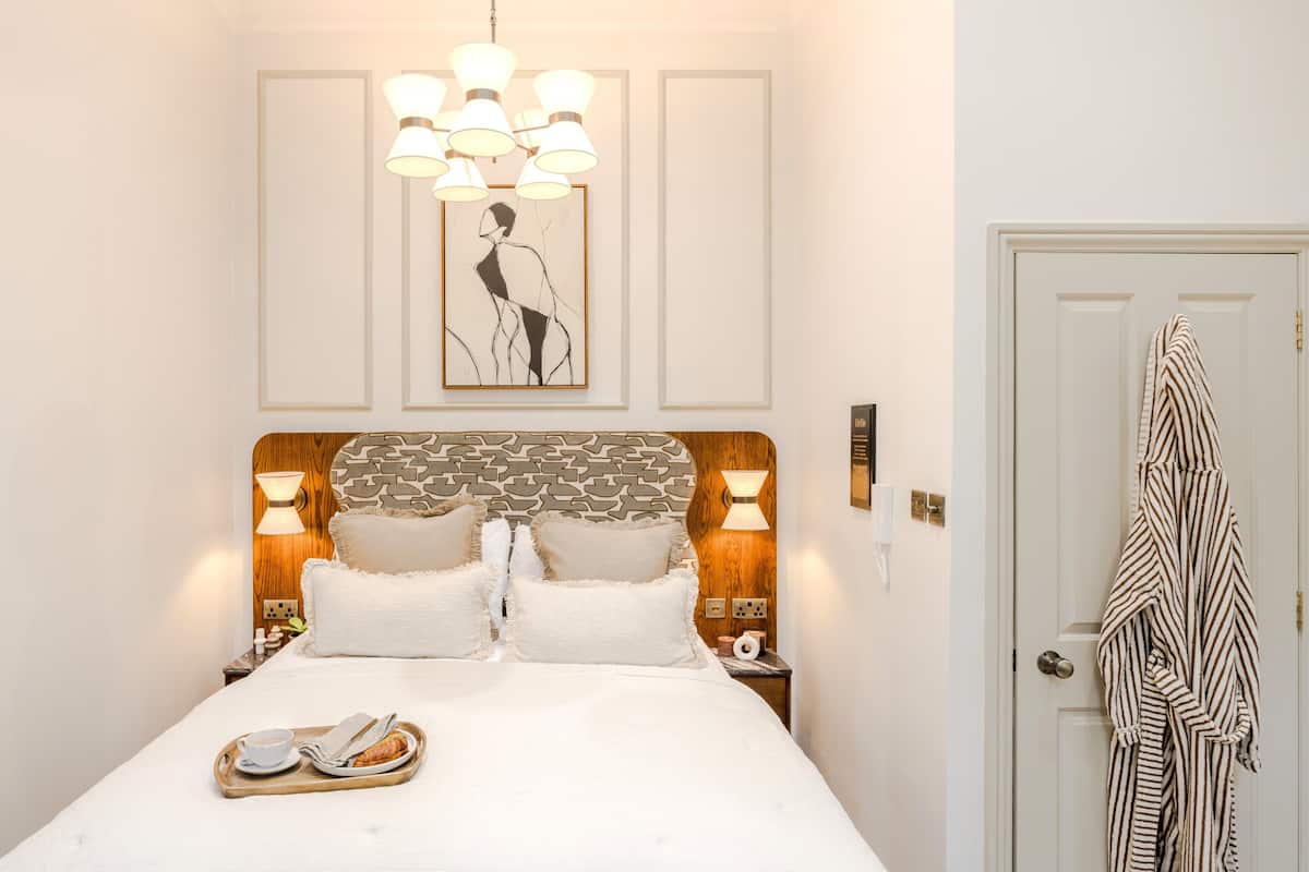 A neatly made bed with a tray of breakfast items, a wall-mounted artwork, and a striped bathrobe hanging on a door.