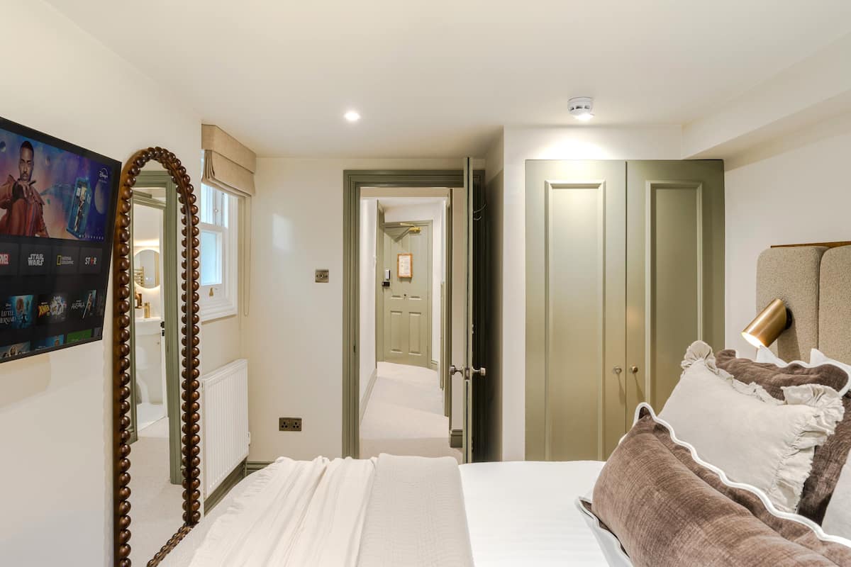 A bedroom with a bed, a mirror, a television, and a door leading to another room.