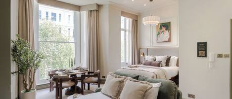 A hotel room with a large bed, a dining table, and a potted plant.