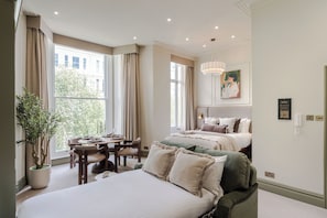 A hotel room with a large bed, a dining table, and a potted plant. - Earl's Court - Your Apartment (London)
