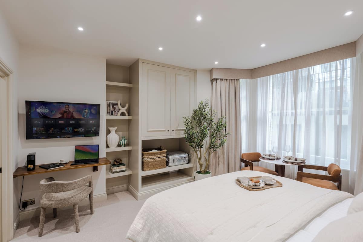 Une chambre d’hôtel comprenant un lit, un bureau avec un ordinateur portable, une télévision, une plante et un coin repas avec des chaises et une table.