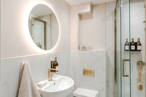 Une salle de bain moderne avec un miroir rond, un lavabo, une douche et des articles de toilette fixés au mur.