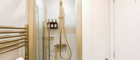 A walk-in shower with a glass door, a towel rack, and a bottle of shampoo.