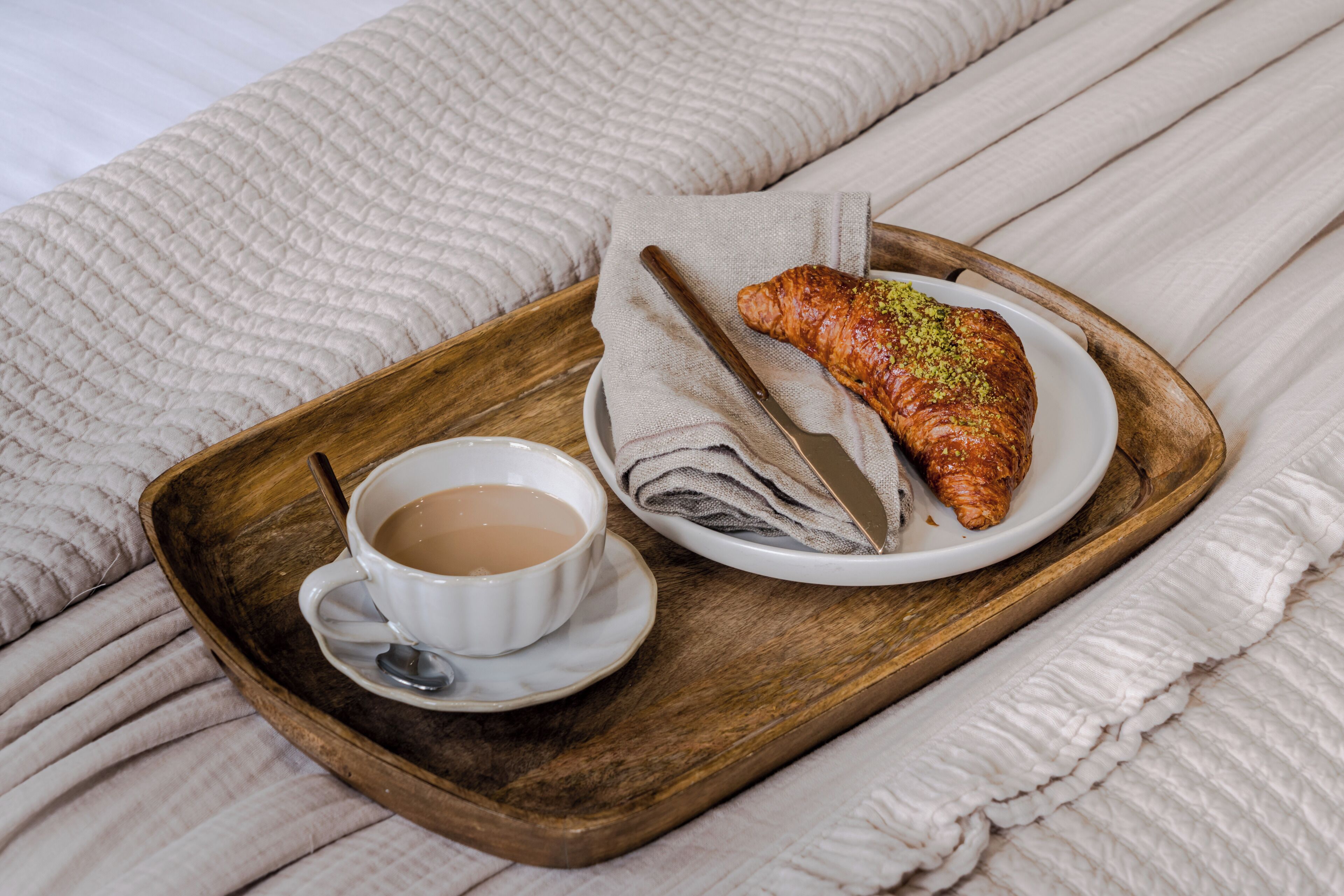 Un plateau avec une tasse de thé et une pâtisserie, posé sur un lit recouvert d’une couverture à motifs.