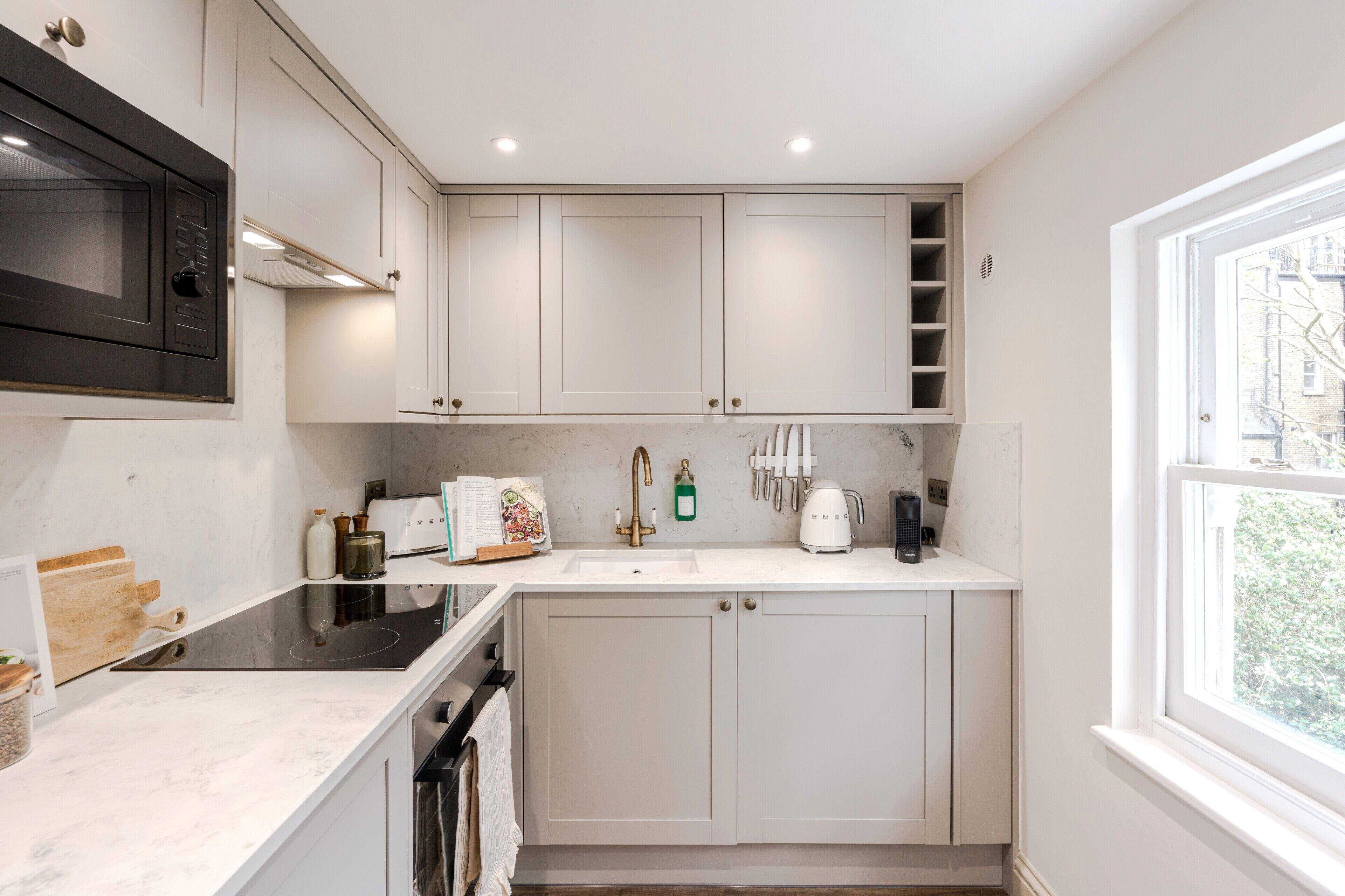 A modern kitchen with white cabinetry, a built-in microwave, and a window providing a view of the outside.