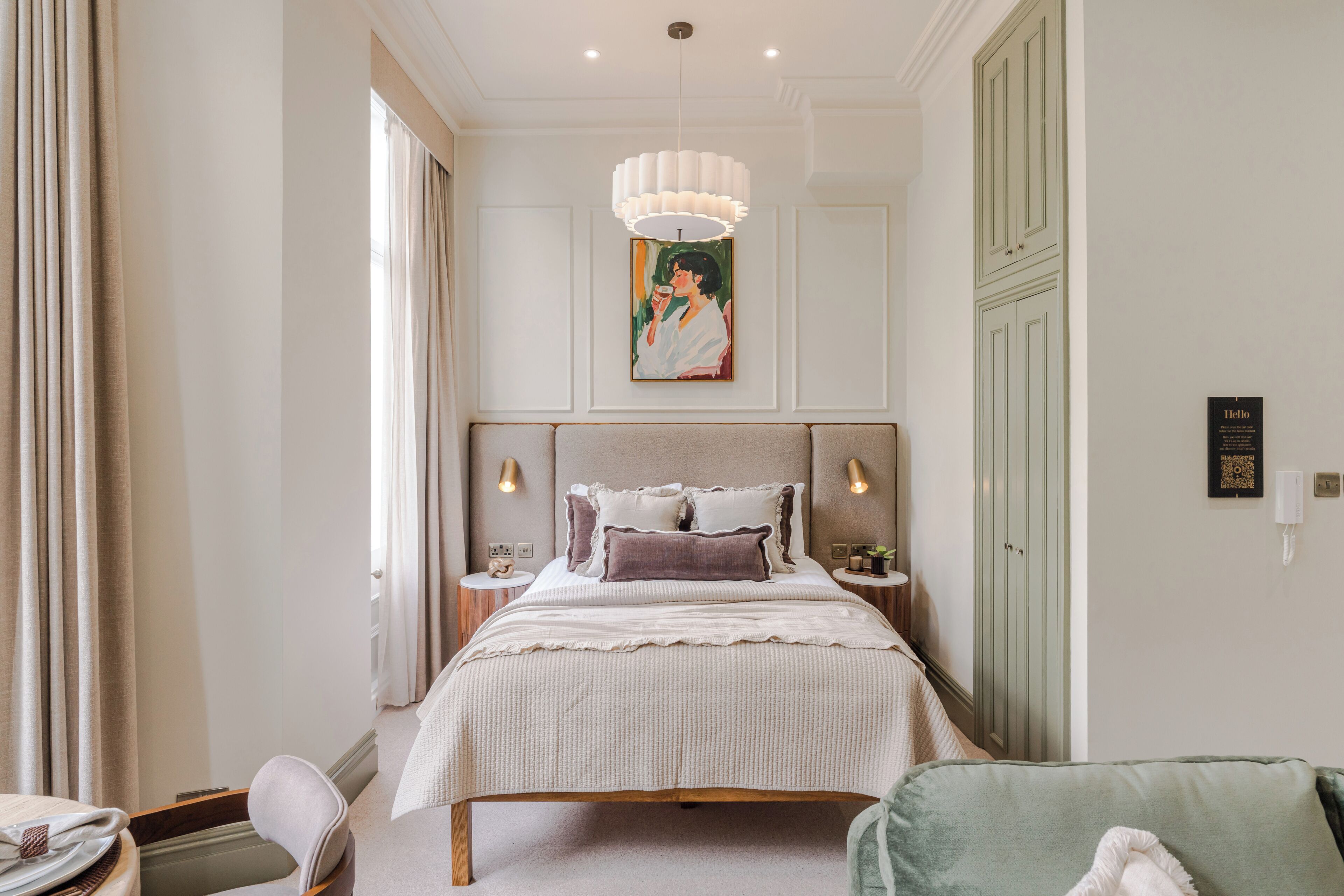 A bedroom with a bed, bedside tables, a hanging light fixture, a painting, and a wardrobe.