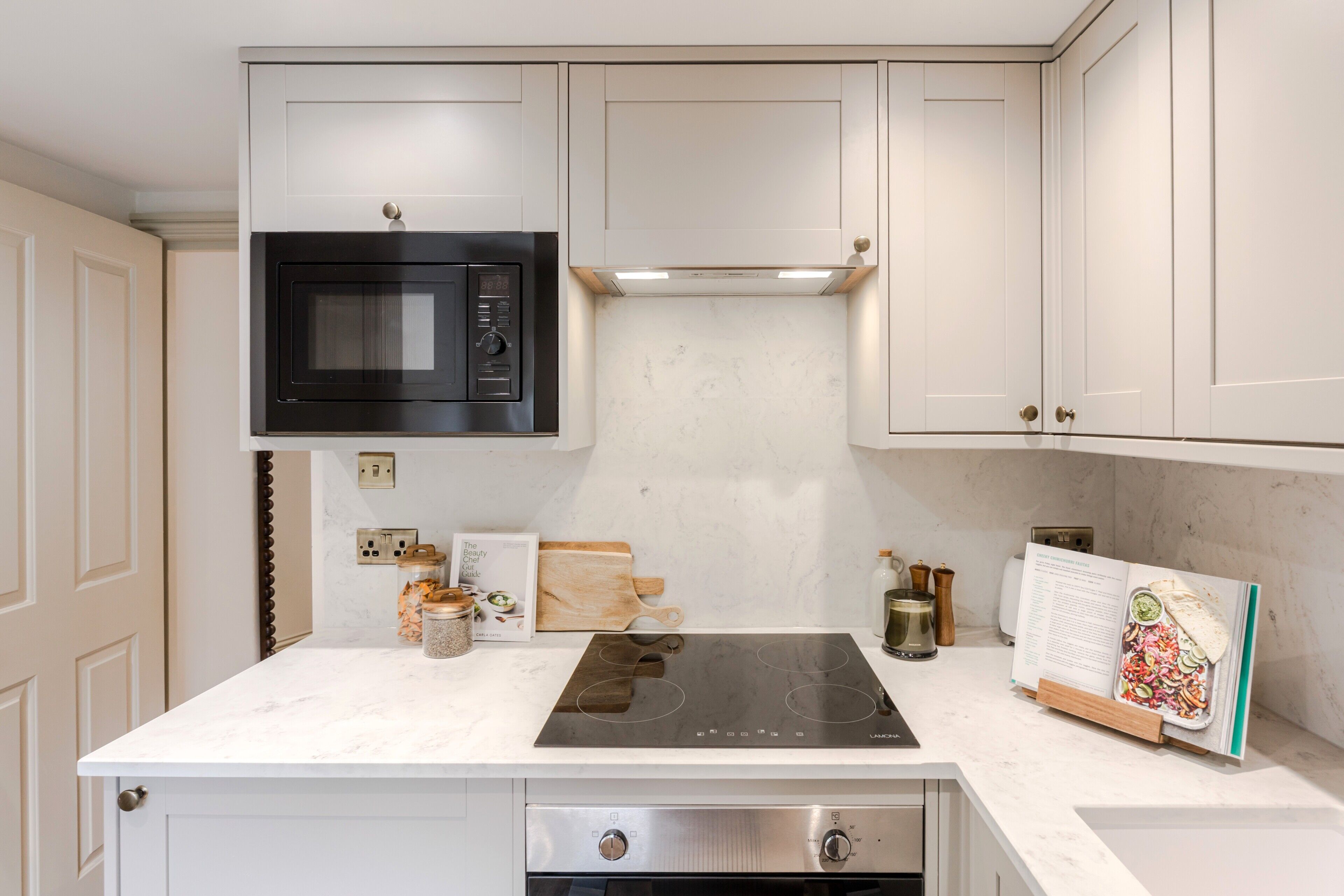 A kitchen with white cabinets, a black microwave, a stainless steel stove, and a cookbook on the counter.