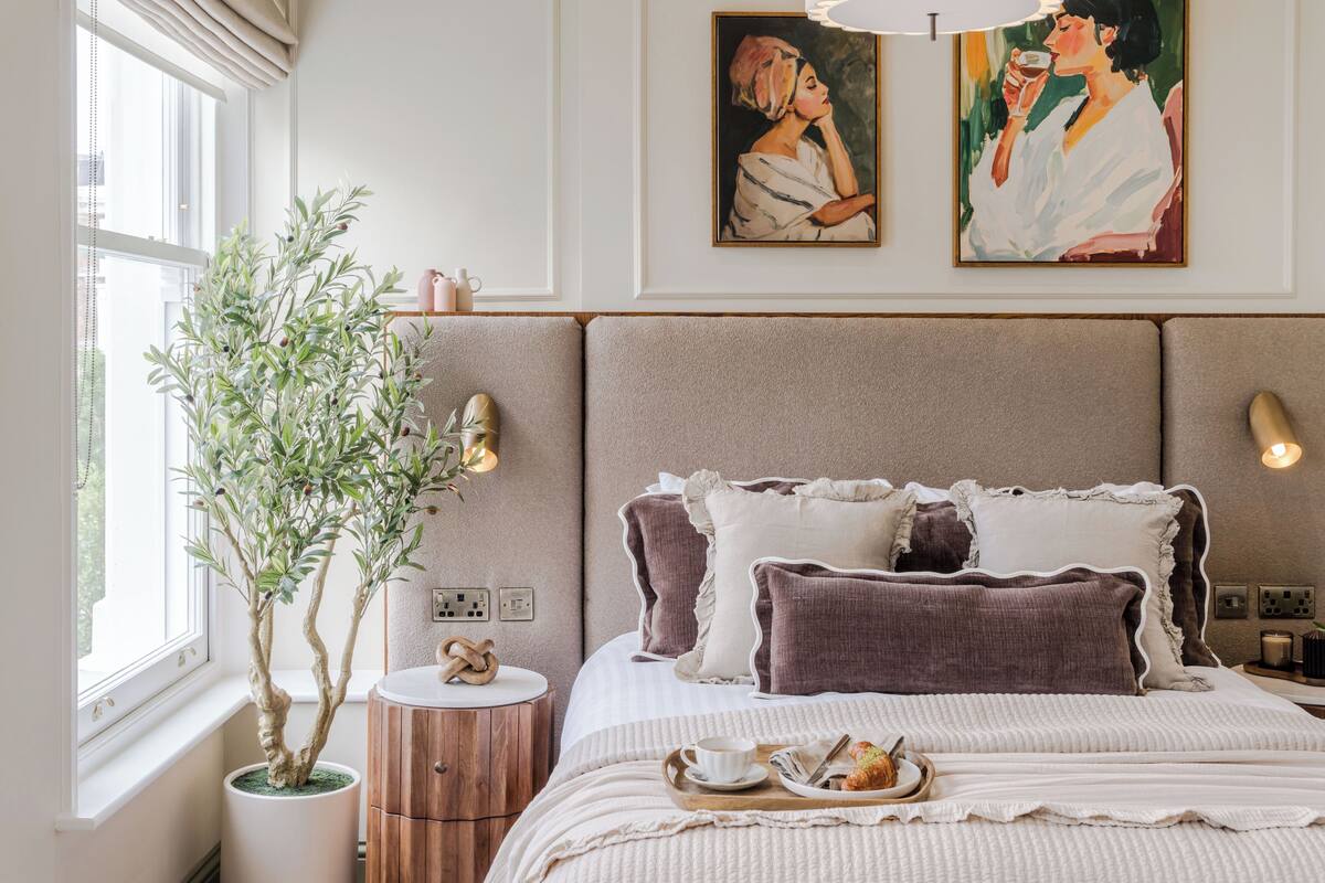 A bedroom with a bed, bedside table, lamp, and a potted plant.