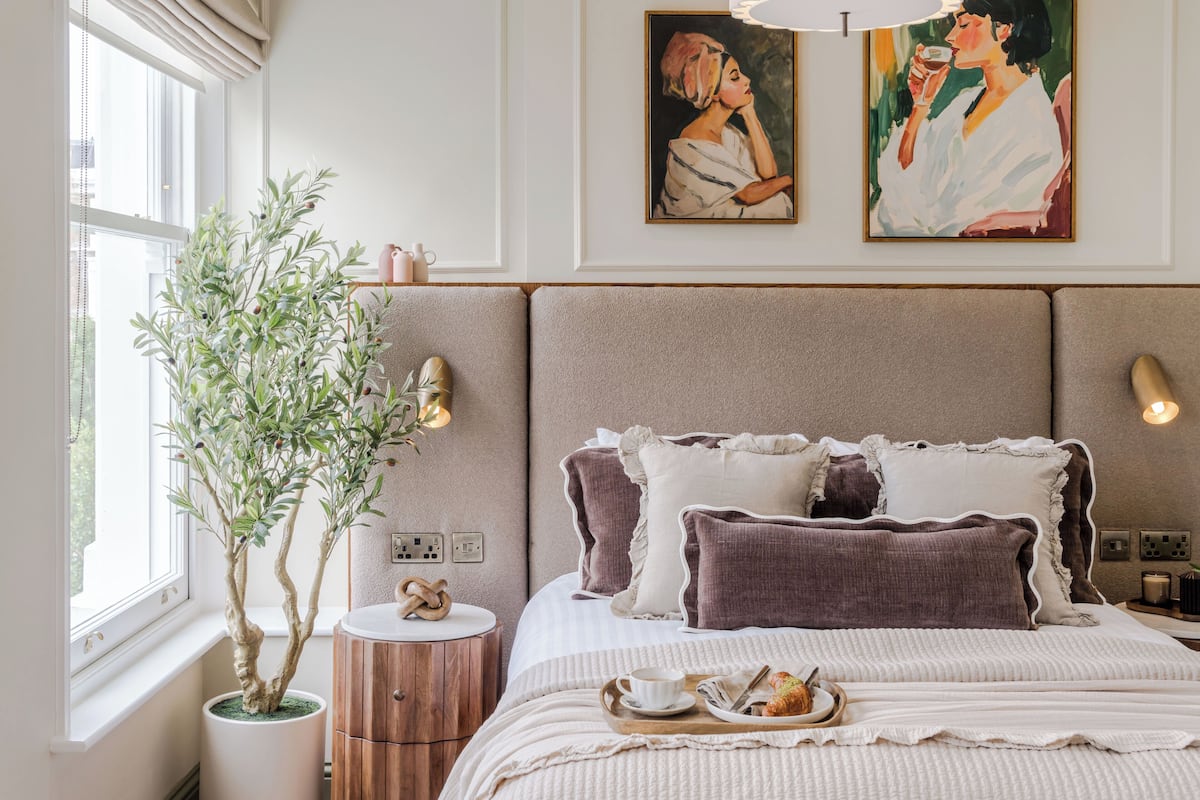 Une chambre à coucher avec un lit, une table de chevet, une lampe et une plante en pot.