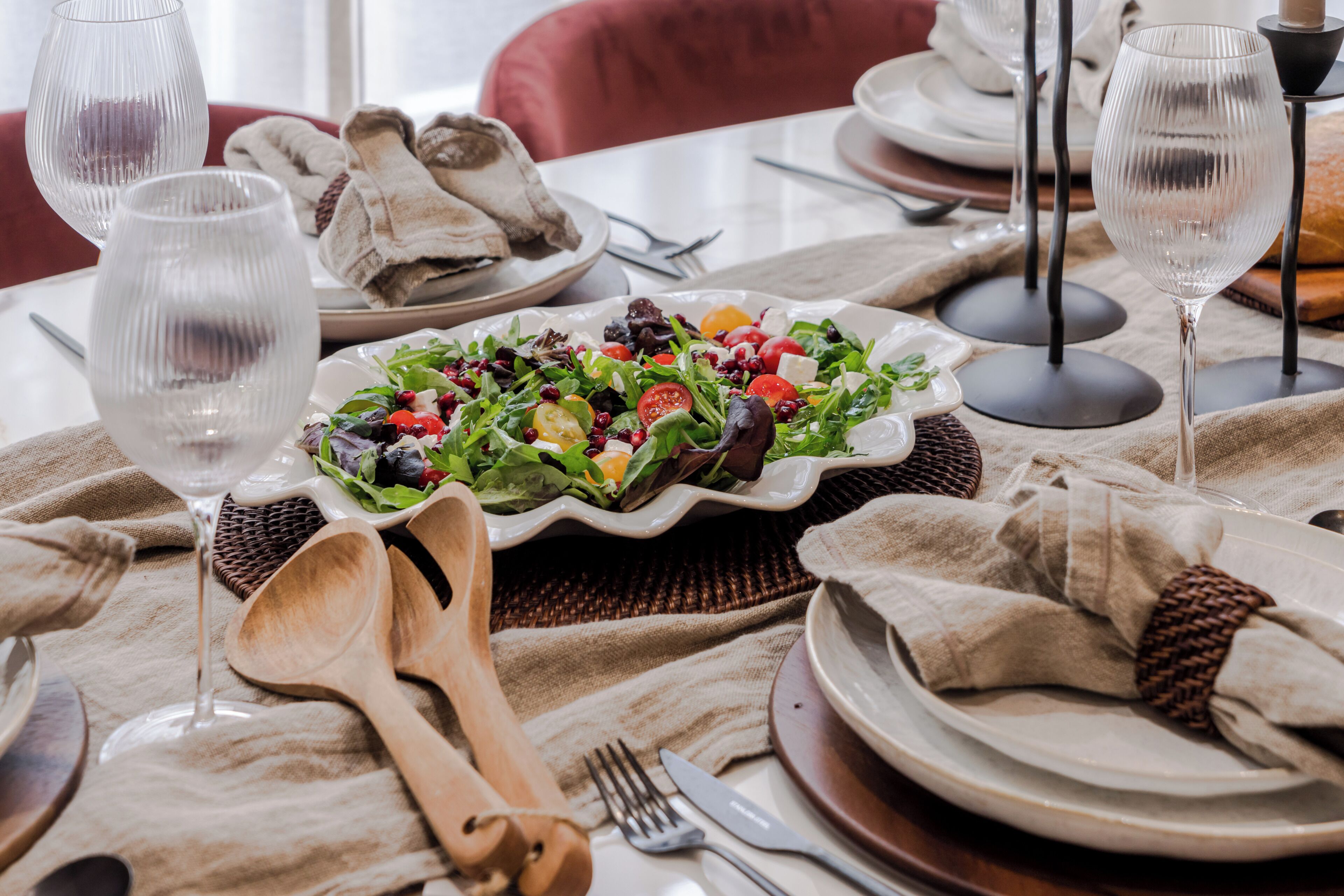 A dining table set with plates, glasses, and cutlery, a salad on a plate, and a woven placemat.