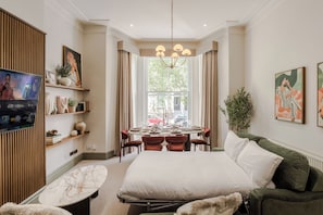 Une chambre d’hôtel comprenant un lit, une table à manger avec des chaises, un téléviseur et des œuvres d’art accrochées aux murs.