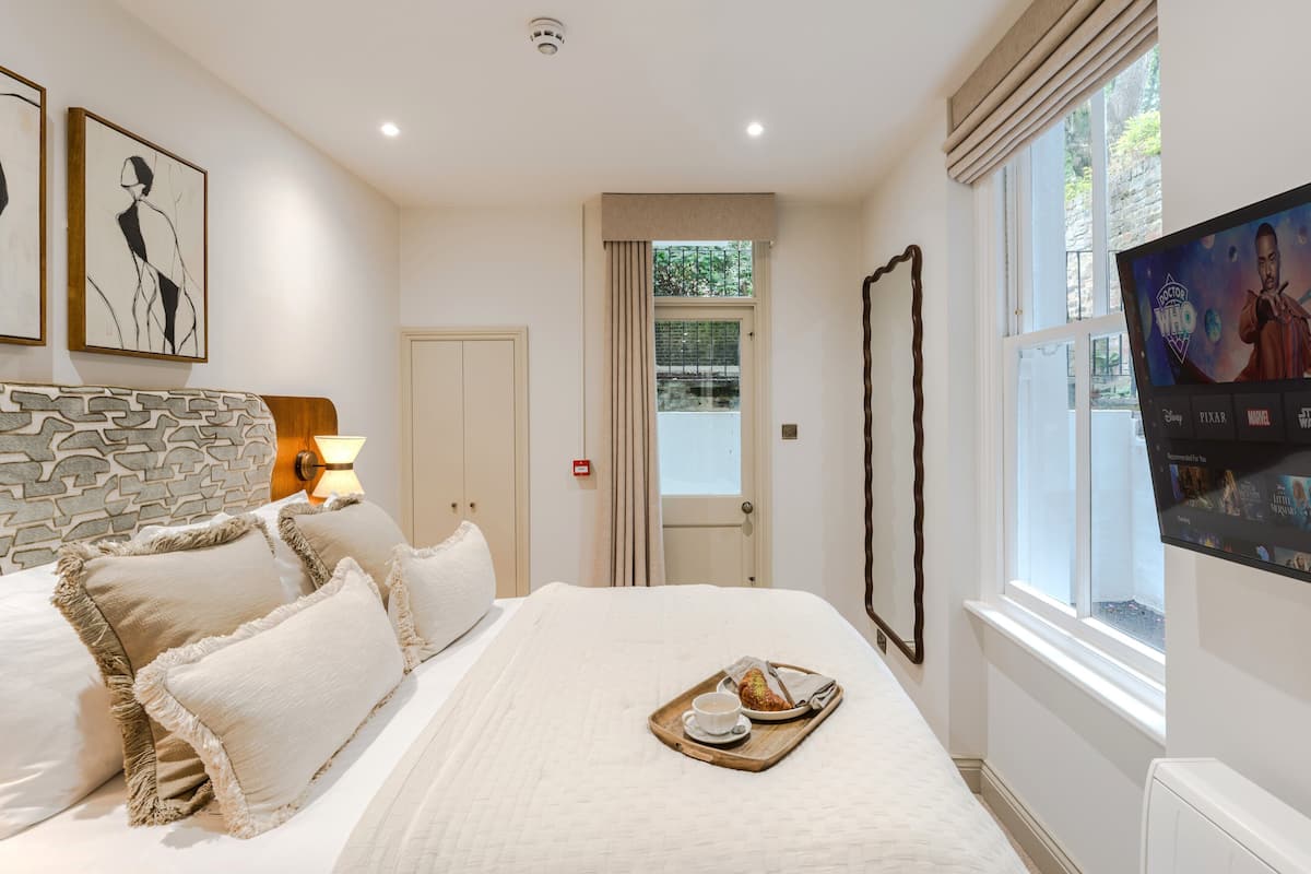 A hotel room with a bed, a tray with a pastry, a TV screen, and artwork on the wall.