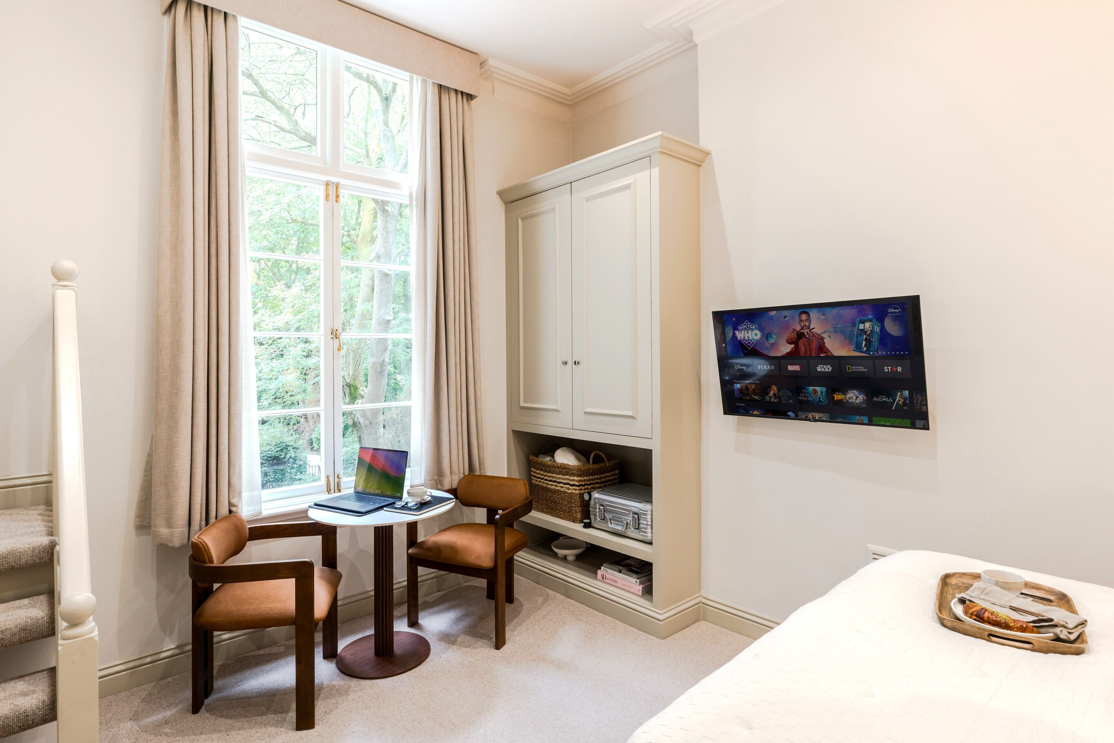 Ein Zimmer mit einem Bett, einem Schreibtisch mit Laptop, zwei Stühlen, einem Kleiderschrank und einem Fernseher.