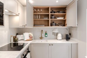 Une cuisine moderne avec des meubles blancs, un four encastré, un évier et un plan de travail sur lequel se trouvent une machine à café et une bouilloire.