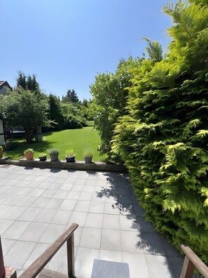 Eine Terrasse mit Fliesenboden, Kübelpflanzen und einem großen immergrünen Baum.