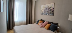 Ein Hotelzimmer mit Bett, Vorhängen, einem Gemälde und einem Nachttisch.