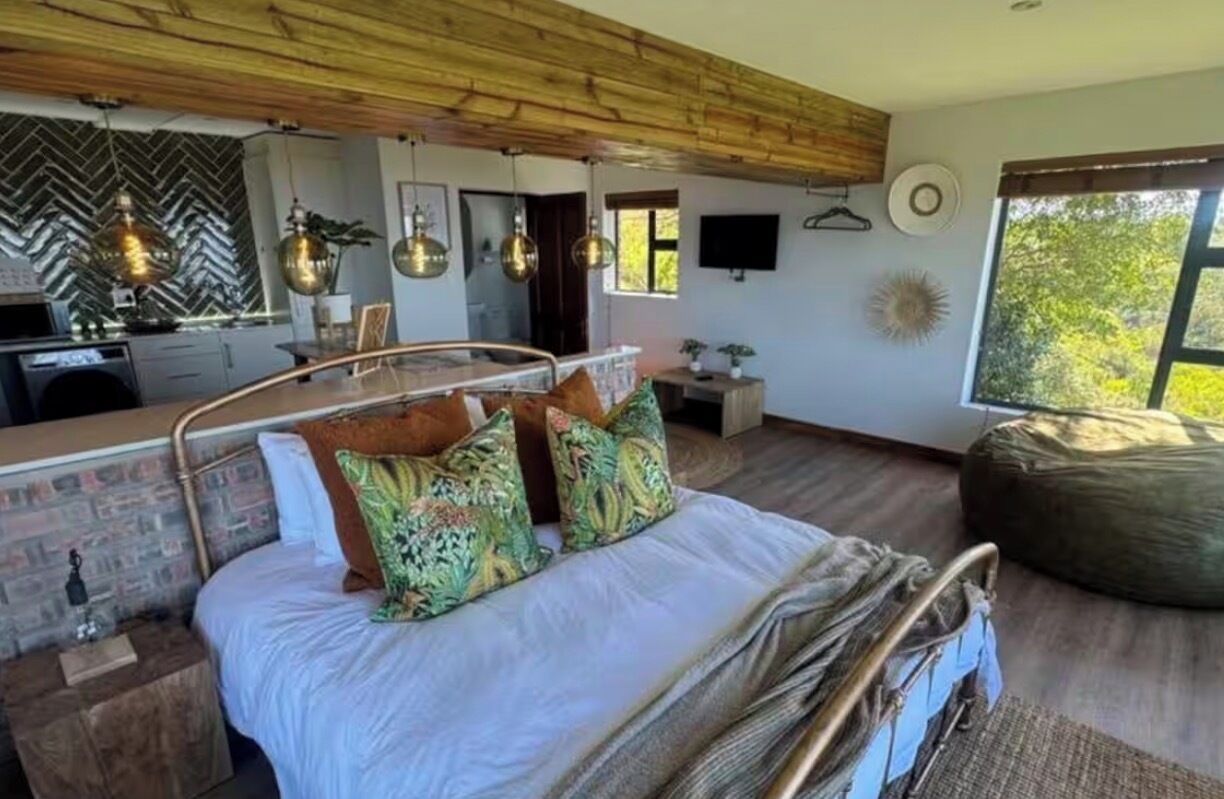 A bedroom with a bed, a wooden ceiling, a window, and a view of trees.