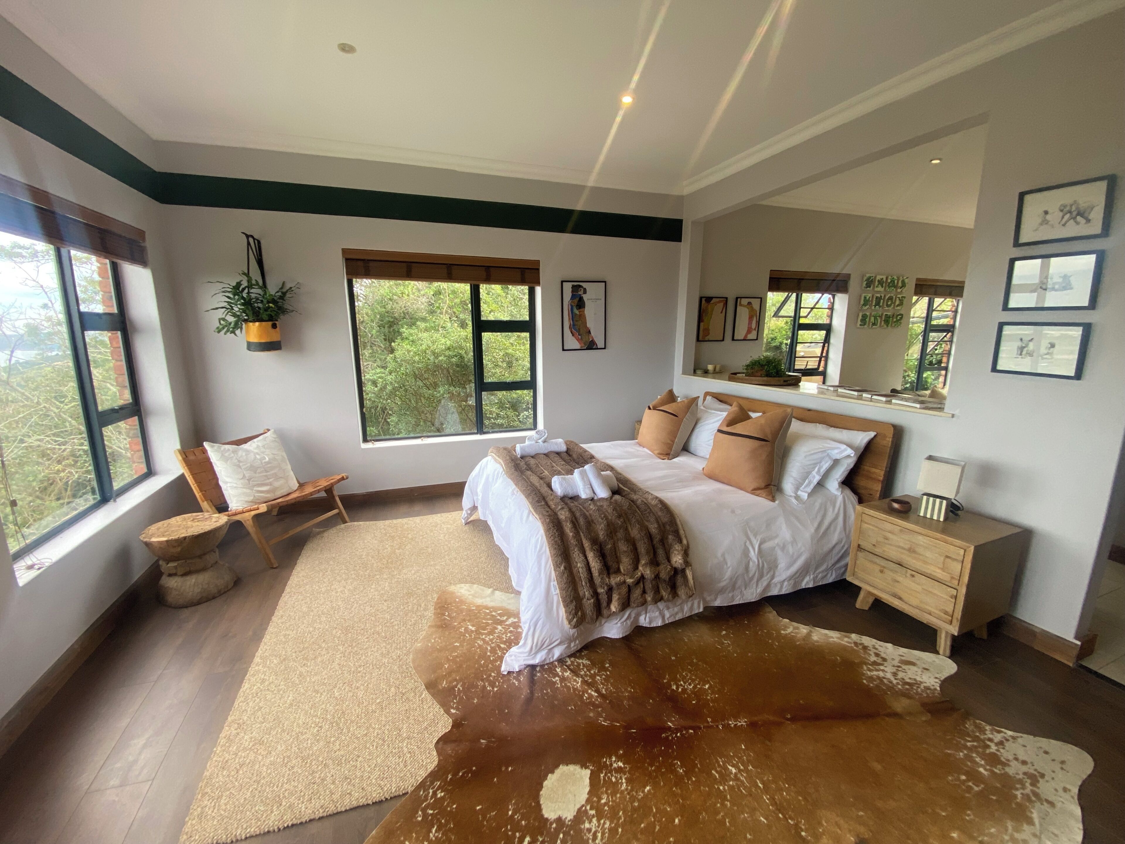 A bedroom with a large window, a bed with a cowhide rug, a wooden nightstand, and a mirror.