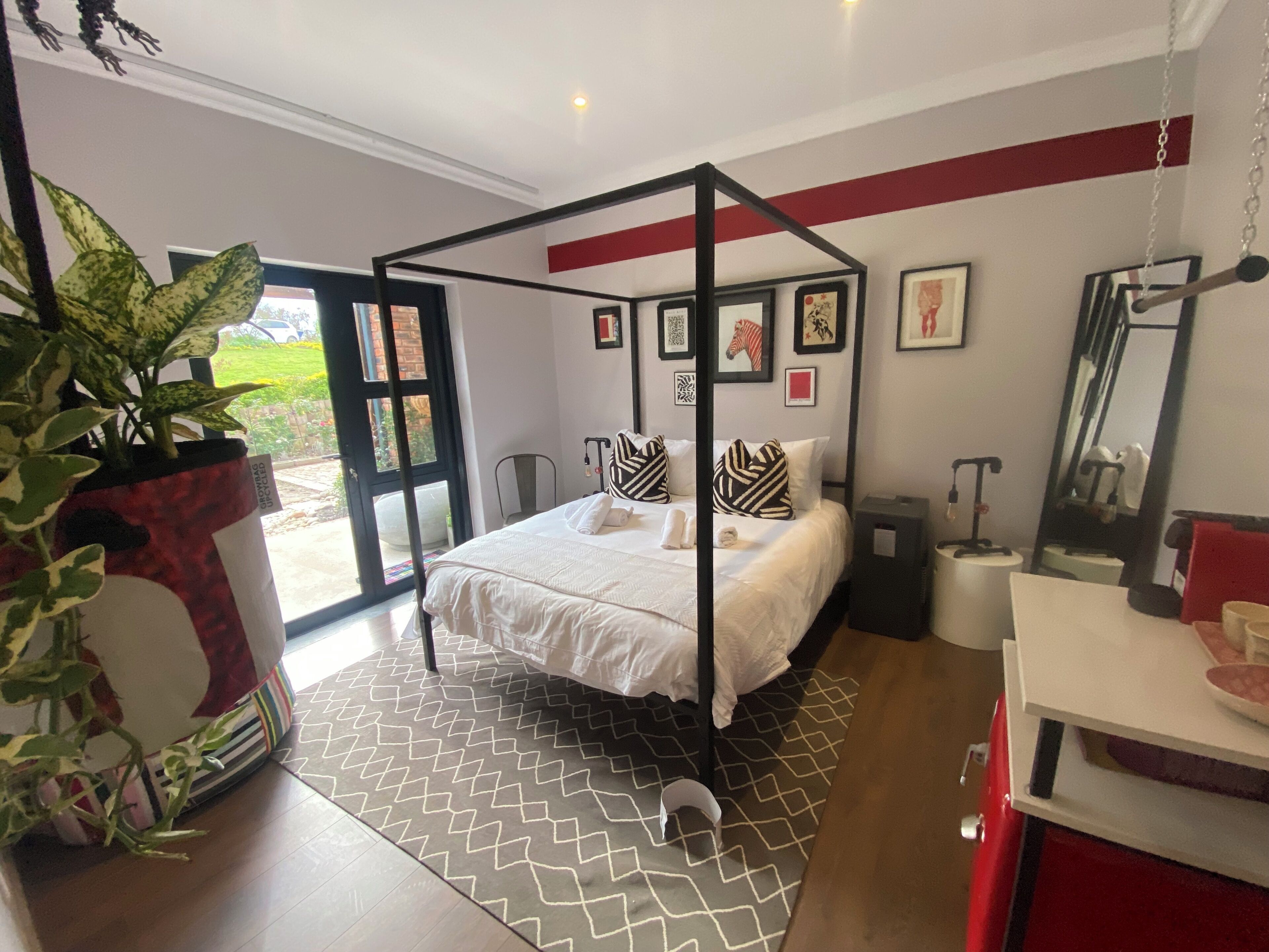 A four-poster bed with a geometric-patterned rug, a potted plant, and framed artwork on the walls.