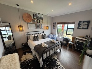 A bedroom with a bed, bedside tables, a desk, a chair, a heater, a window with a view, and wall art. - The Liora (hoekwil)